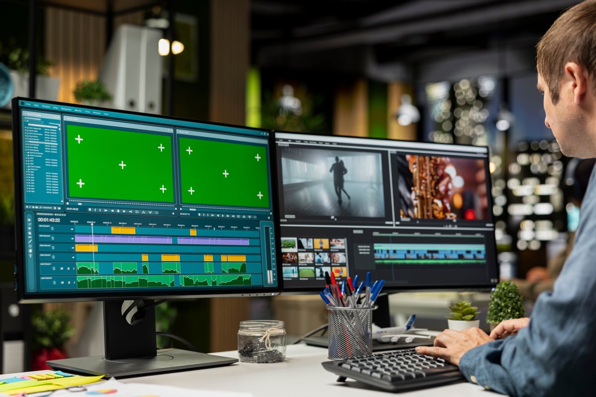 Professional editor working in video production with chroma key at agency office, doing color grading and creating a montage on dual monitors