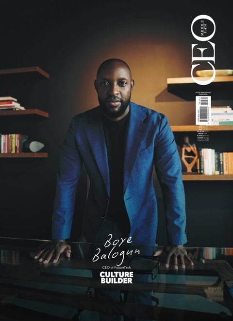 Portrait of Boye Adefemi-Balogum in a blue blazer leaning against a desk in front of bookshelves, labeled as Culture Builder