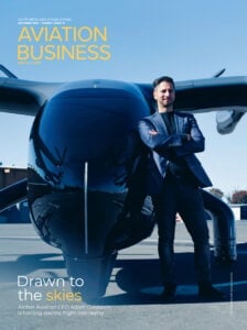 Man in flight suit leaning against large blue aircraft on tarmac, Aviation Business magazine cover