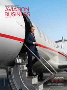 Businessman in dark suit boarding aircraft via stairs, with Aviation Business magazine cover visible on fuselage