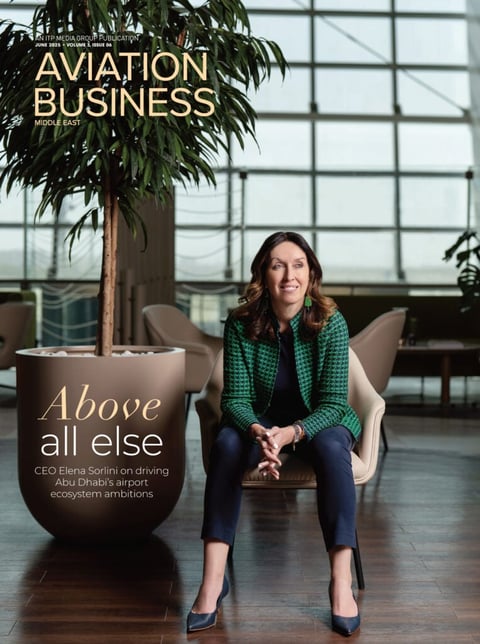 Woman in green jacket seated in modern airport terminal with potted plant and glass windows, Aviation Business magazine cover